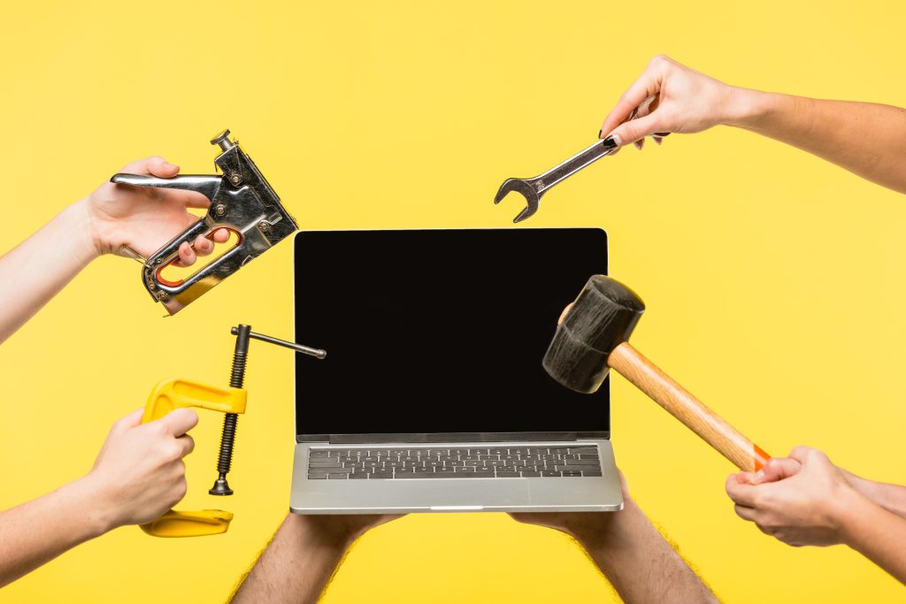 cropped shot of hands holding tools and laptop with blank screen isolated on yellow